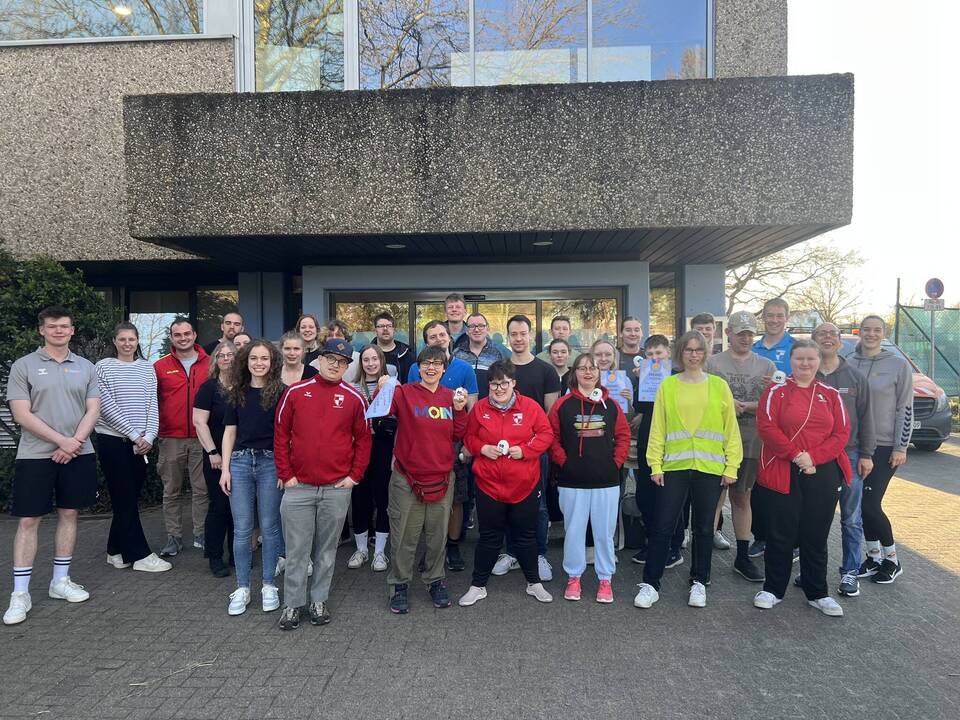 Die Athletinnen und Athleten stehen in Reihen nebeneinander vor dem Schwimmbad.